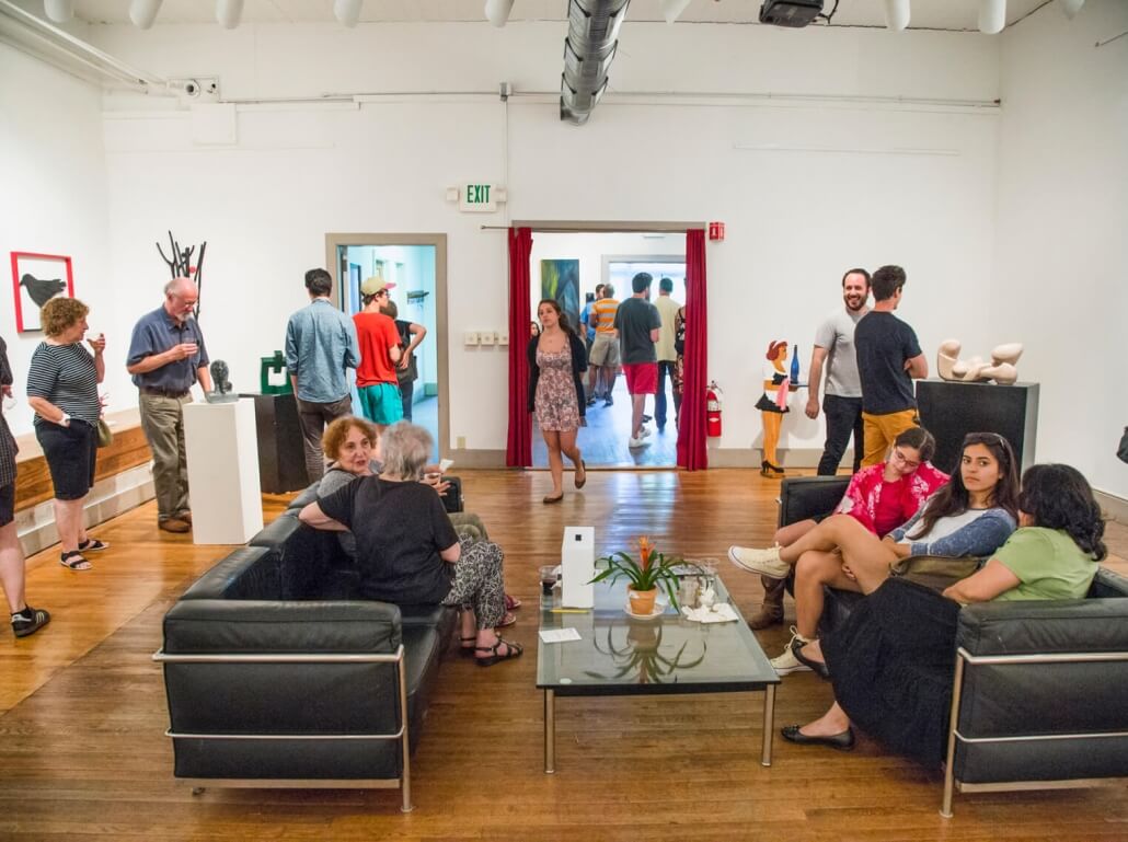 ASK's member's gallery, full of art viewers, with art hanging on the walls, with two couches and a coffee table