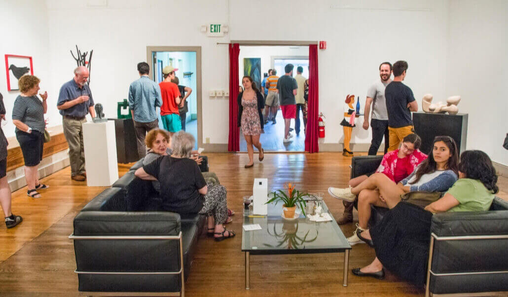 ASK's member's gallery, full of art viewers, with art hanging on the walls, with two couches and a coffee table